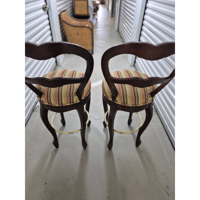 These are Victorian-style carved mahogany balloon-back swivel bar stools featuring multi-colored striped fabric upholstery...