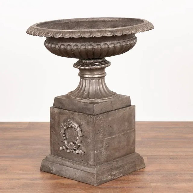 This pair of generous sized cast iron urns resting on a square plinth have been sand-blasted, resulting in an attractive...