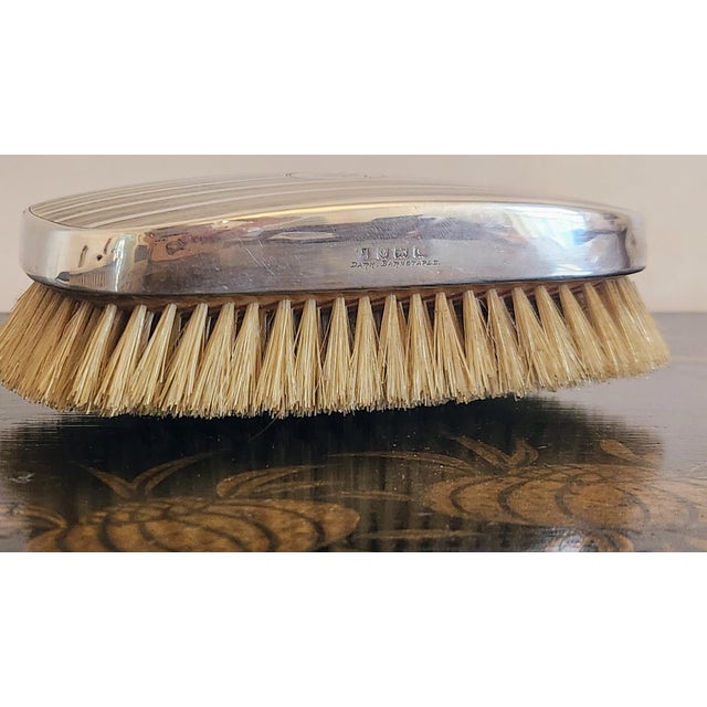 A refined English sterling silver grooming trio consisting of a hair brush, clothes brush, and comb, all engine turned and...