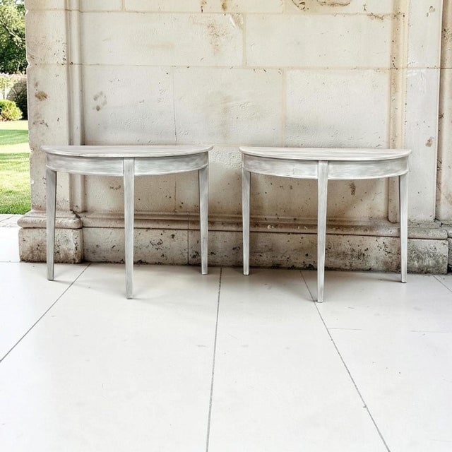 A pair of 19th century French Directoire demi lune consoles in solid oak, finished in a soft whitewash that lets the...