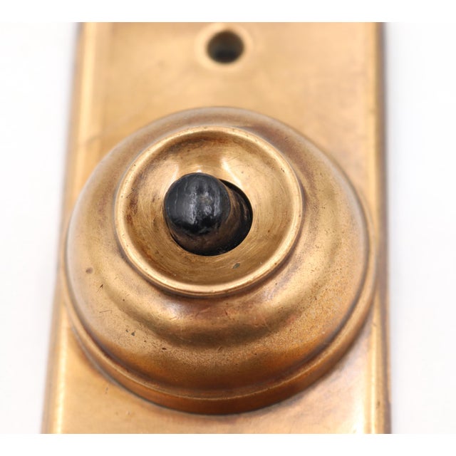 Vintage polished brass doorbell plate with a single black plastic button. The original mounting screws are not available....