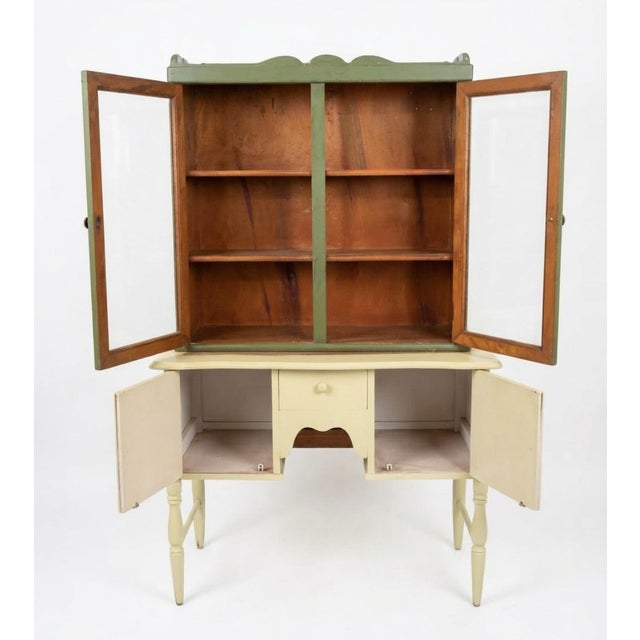 Charming vintage painted kitchen hutch featuring a two-piece look with a glass-front display cabinet above and enclosed...