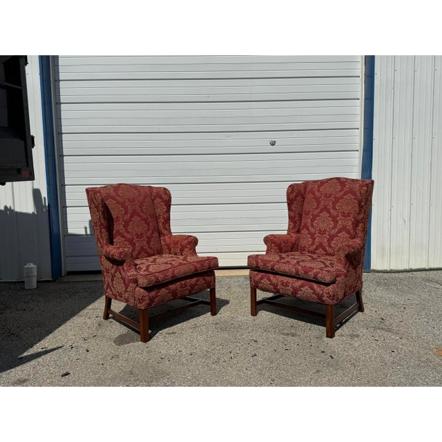 A handsome pair of Chippendale-style fireside wingback chairs featuring classic high backs, sculpted wings, rolled arms,...