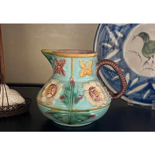 Victorian majolica pitcher, bulbous at the bottom with molded flower forms and a rope form handle. The rim is yellow with...