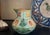 Victorian majolica pitcher, bulbous at the bottom with molded flower forms and a rope form handle. The rim is yellow with...
