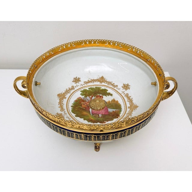An elegant antique porcelain and gilt bronze centerpiece bowl featuring a finely hand-painted romantic courting scene,...
