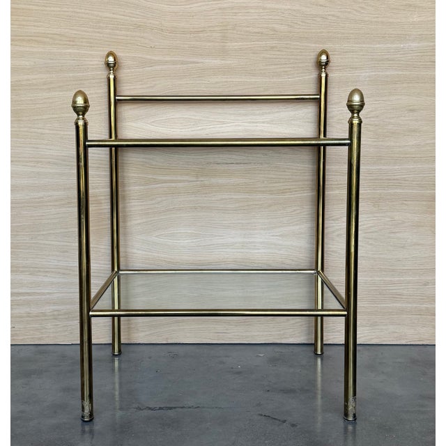 Pair of midcentury Italian two tier brass and glass nightstands with crest. Simple tables with a low grid shelve and glass...