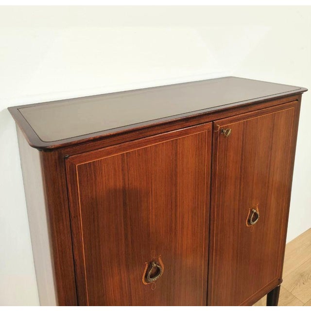 Elegant bar cabinet, designed by Paolo Buffa. The wooden frame features inlaid doors and brass details, and the top is...