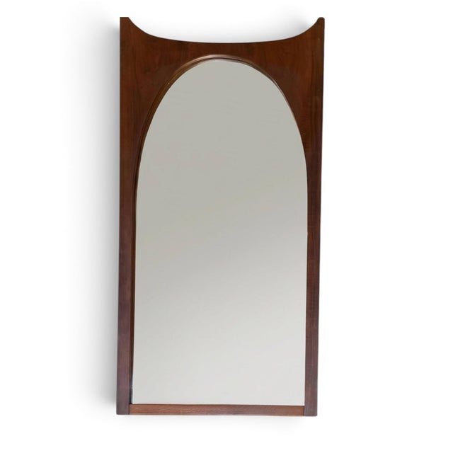 Mid-century sculpted walnut wall mirror. Arched glass set into a solid walnut frame with a concave scooped top rail and...