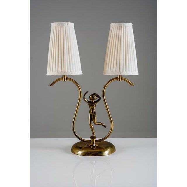 Elegant Swedish Modern table lamp crafted in brass, featuring a sculptural central figure and two gracefully curved arms....