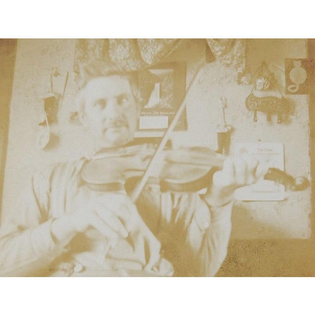 Early 20th century sepia toned albumen photograph snapshot of a man in his house playing a fiddle or violin. Lots of odd...