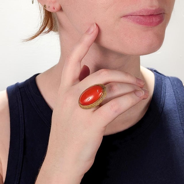 A fine vintage gold & coral ring. In 18 karat yellow gold. With a central bezel-set coral cabochon in a figural braided...