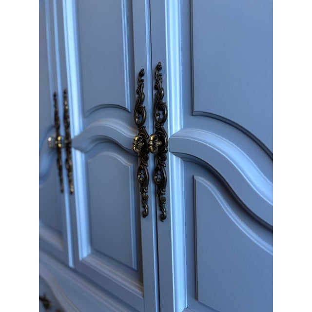 Elegant French Provincial–style armoire refinished in a soft blue tone, featuring graceful curves, paneled doors, and...