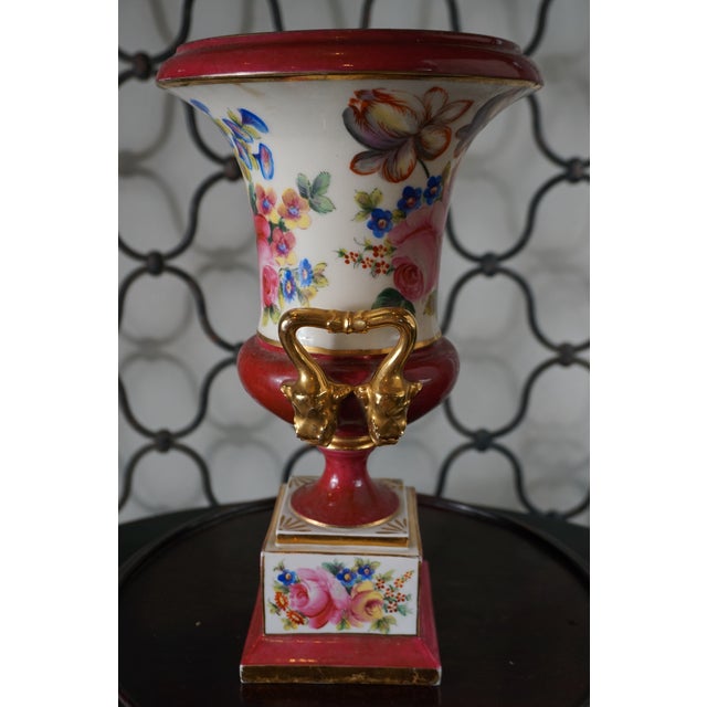 A striking vintage porcelain urn featuring richly saturated oxblood red accents, hand-painted floral decoration, and...