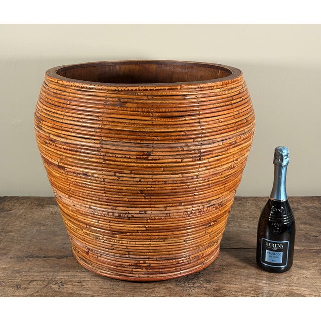 This oversized vintage planter features a tapered cylindrical form constructed from wrapped pencil reed / rattan coils...