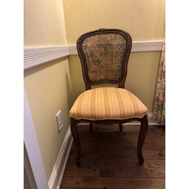 A charming pair of Louis XV-style caned side chairs featuring hand-carved walnut frames with delicate floral and foliate...
