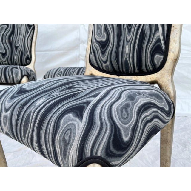 Group of four silver gilt dining chairs made of wood. The black gray and white fabric lends a nod to Pucci. The material...