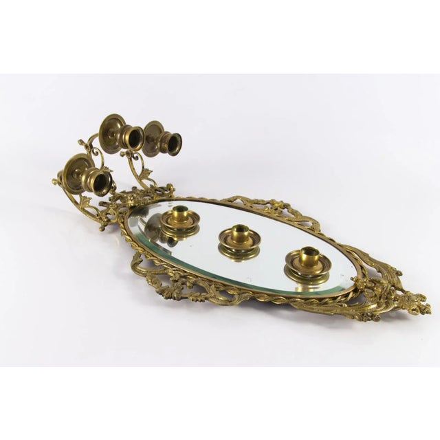 This Louis XVI style mirror has a bronze frame surrounding a beveled oval mirror plate. The frame is decorated with...