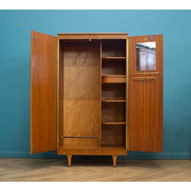 Mid-century wardrobe in teak with inset handles and tapered legs. Hanging rail to the left, shelves with pull-out tray to...