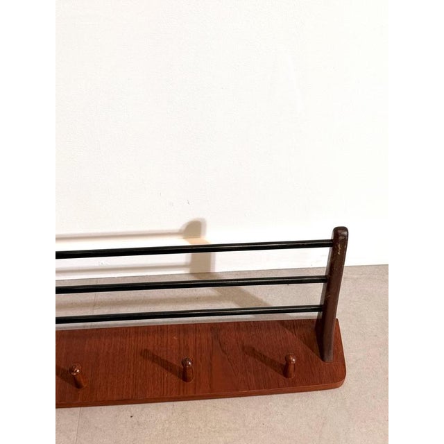 Elegant mid-century modern wall coat rack featuring a warm teak wooden base combined with sleek black metal bars and...