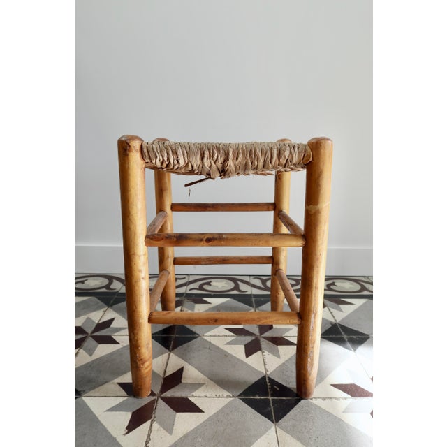 A charming antique low stool with a rustic feel, featuring a honey-yellow wooden frame and a beautiful woven straw seat....