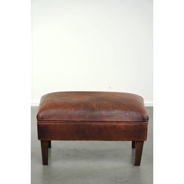 This vintage ottoman is made of sheepskin in a brown color scheme with a timeless look. The ottoman shows some signs of...