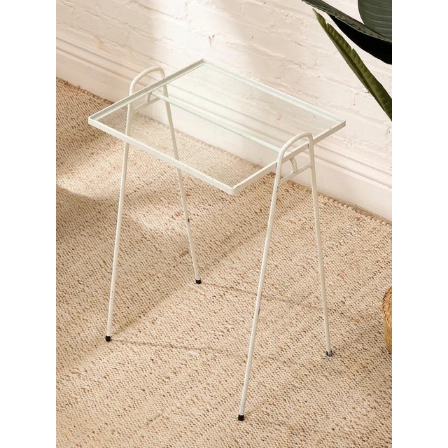 charming vintage tray table with a slender white-painted metal frame and rectangular clear glass top. The raised perimeter...