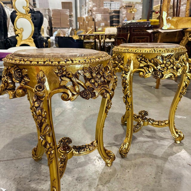 A beautifully ornate French-style side table featuring an elegant gold-leaf frame and a distinctive beige marble top with...