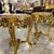 A beautifully ornate French-style side table featuring an elegant gold-leaf frame and a distinctive beige marble top with...