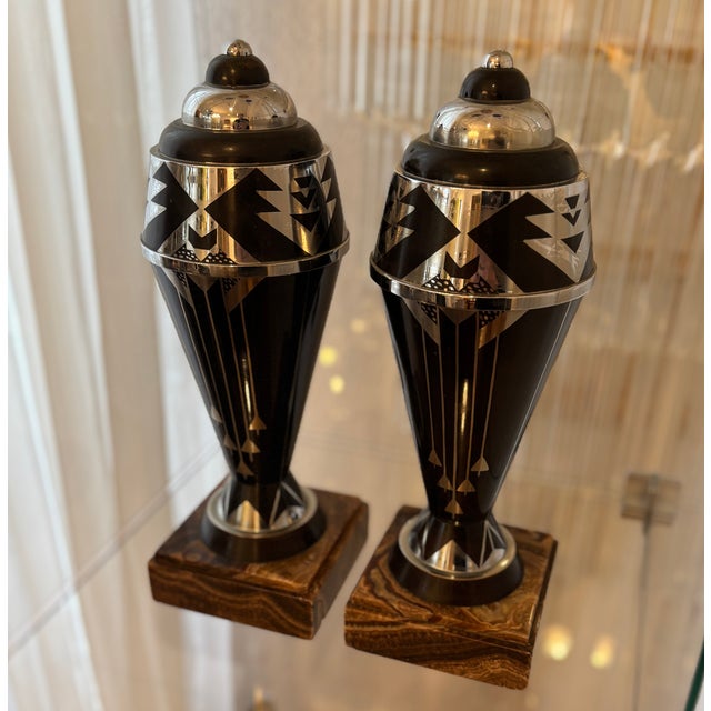 The two vase-shaped decorative objects are designed in a typical, graphic Art Deco pattern using black lacquer and silver...