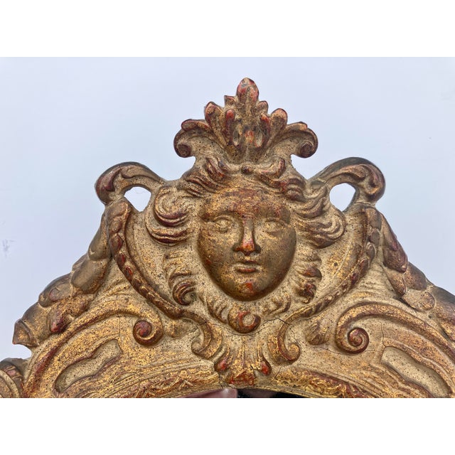 This mirror has foliate designs with a crest that has a lady’s portrait. There is a mellow gold finish and the slightly...
