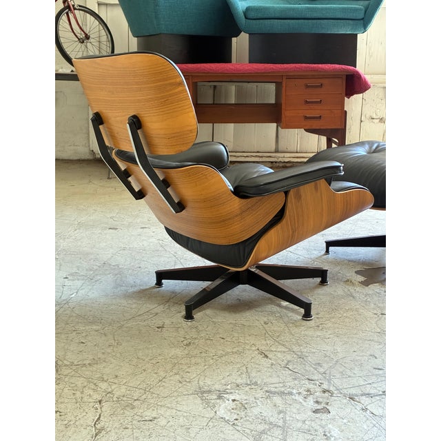 Vintage Herman Miller Charles Eames lounge chair and ottoman, featuring smooth black leather and molded walnut shell...