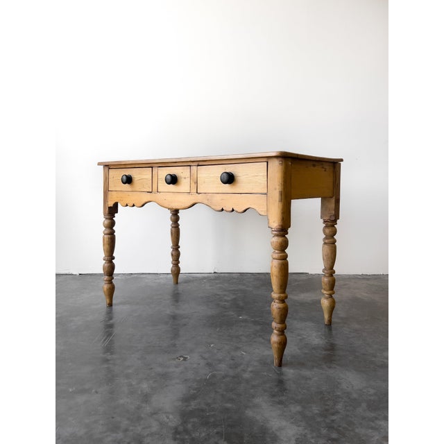 A charming antique 19th century English pine table with a scalloped apron and turned legs. Three drawers with black knobs....