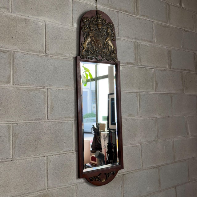 A majestic and imposing vertical wooden wall mirror with a sumptuous heraldic frieze in embossed brass and beveled glass,...
