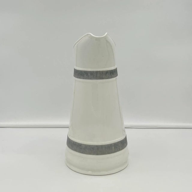 This outstanding white pitcher has a pewter handle and two bands of pewter going around it. A large arching spout is a...