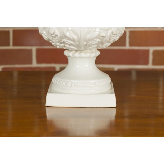 A pair of Blanc de Chine urns from the Midcentury period, with rams heads handles, grapes and ivy motifs. This pair of...