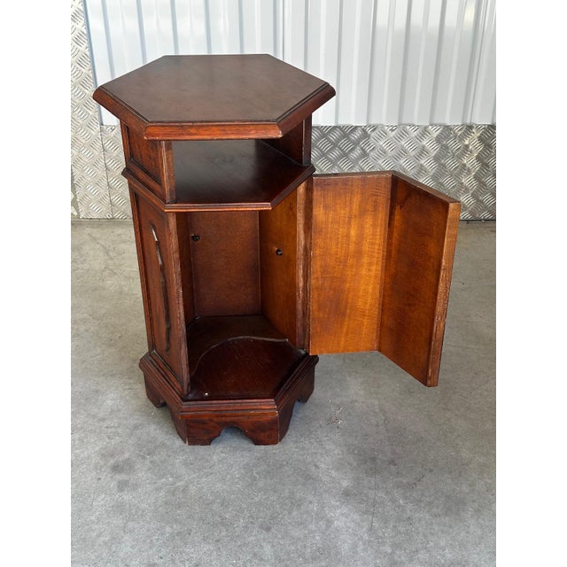 A hexagonal mahogany side table, 20th century. Molded top, open niche, and lower storage compartment with a door. Molded...