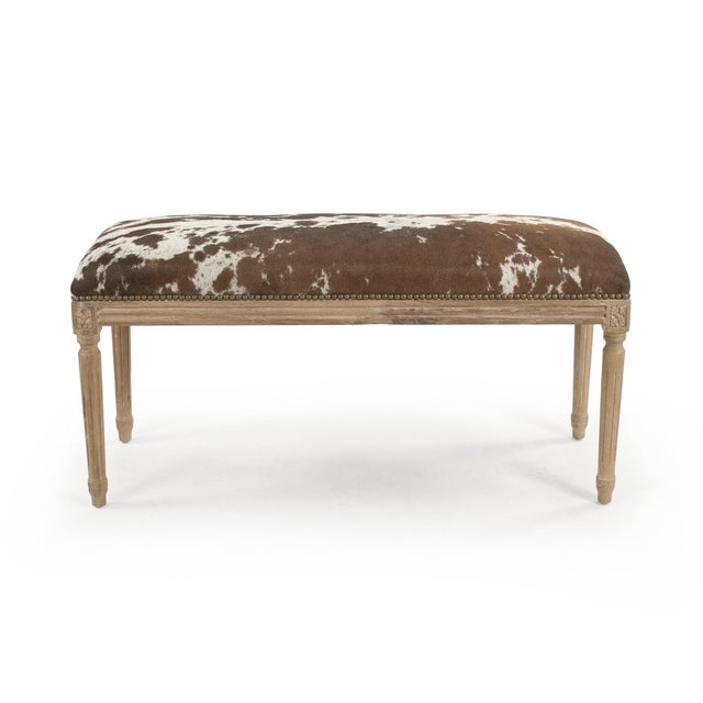 This is a bench featuring a sophisticated design with cowhide upholstery and an oak wood frame. The upholstery showcases a...