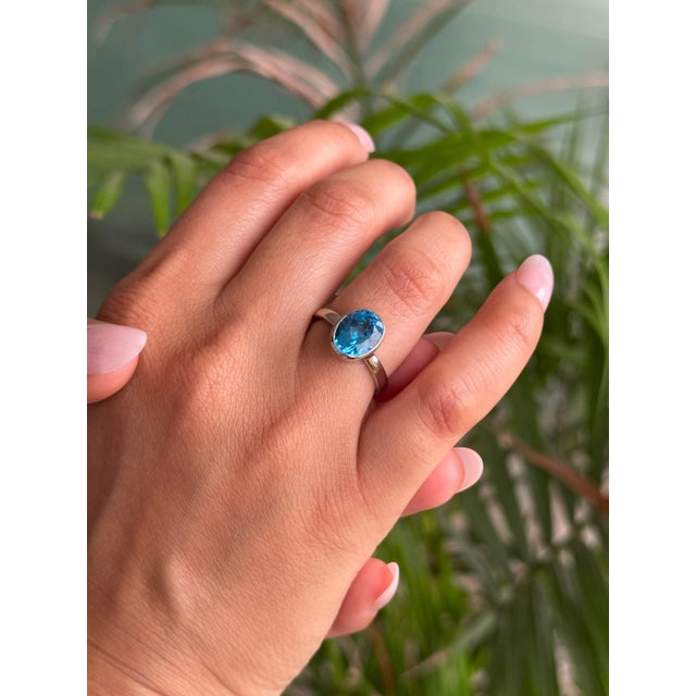This 925 Sterling Silver solitaire ring showcases a bright oval Blue Topaz set securely in a smooth bezel setting. The...