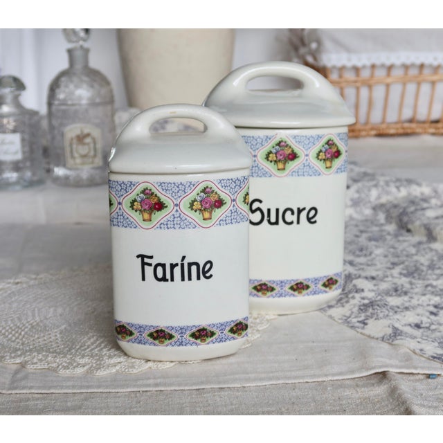 Charming pair of antique earthenware pots, each adorned with a polychrome floral design on an ivory background. Labeled...