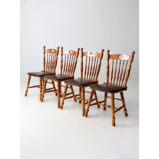 A set of four vintage spindle back dining chairs crafted in warm wood tones with turned legs and a classic silhouette. The...