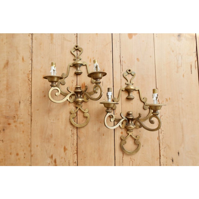 Pair of two-arm brass wall sconces, featuring an elegant design of scrolls and curves inspired by classical style, with a...