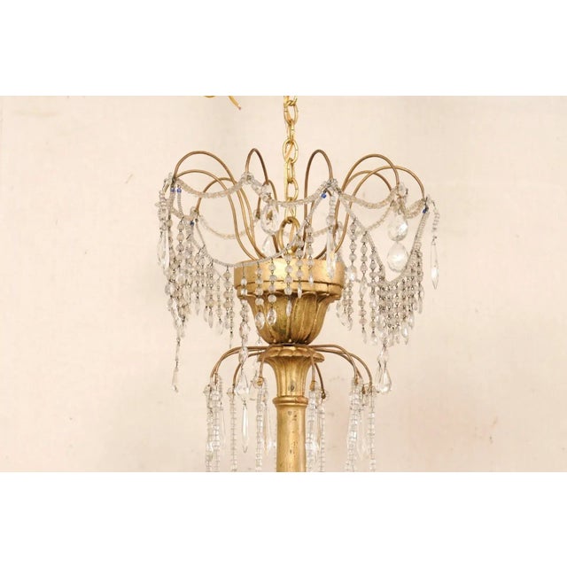 An Italian crystal and gilt-wood column chandelier from the mid 20th century. This mid-century hanging light from Italy...
