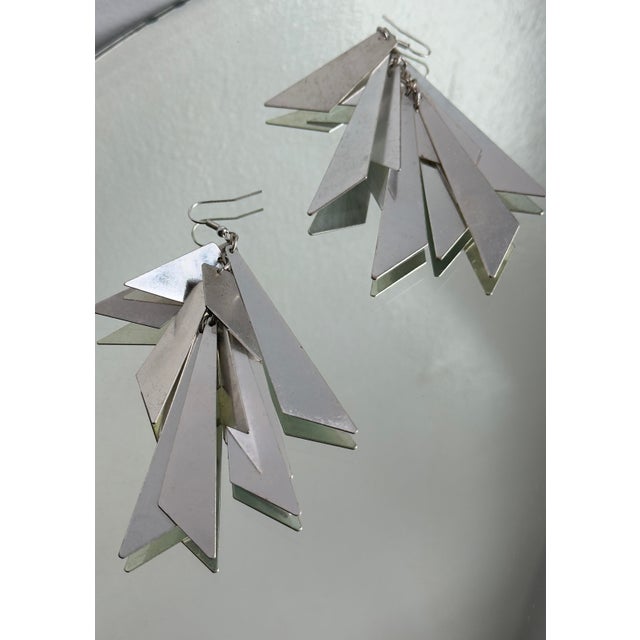 Statement dangle earrings in silver tone, reflective metal with elongated geometric shard elements arranged in a tiered...