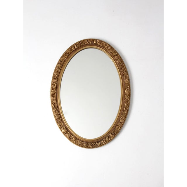 A charming mid-century oval gilt mirror featuring an ornate floral relief frame with elegant French Revival influence. The...