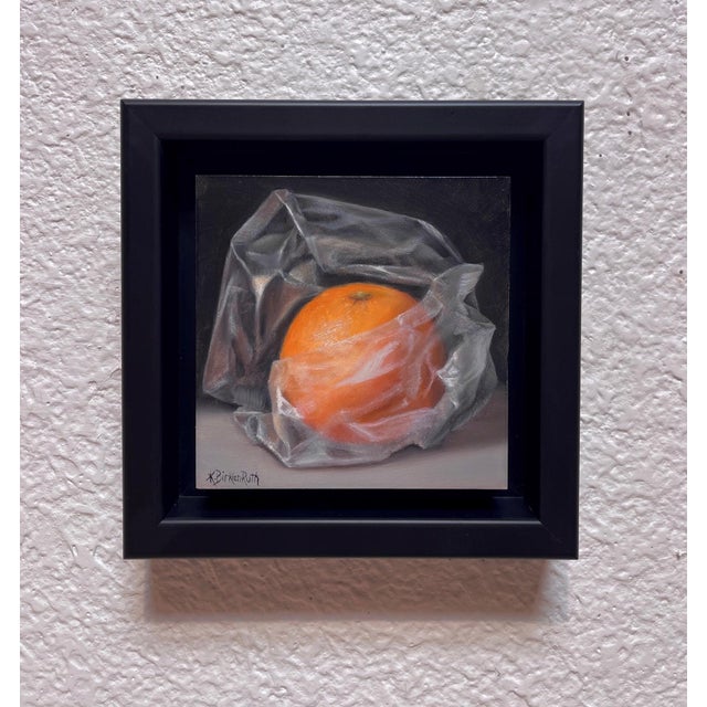 This artwork presents an orange partially enveloped in translucent plastic, creating a striking contrast between the...