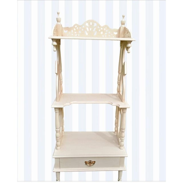A very sweet off white etagere with pretty decorative fretwork details. The etagere has a pullout drawer at the bottom...