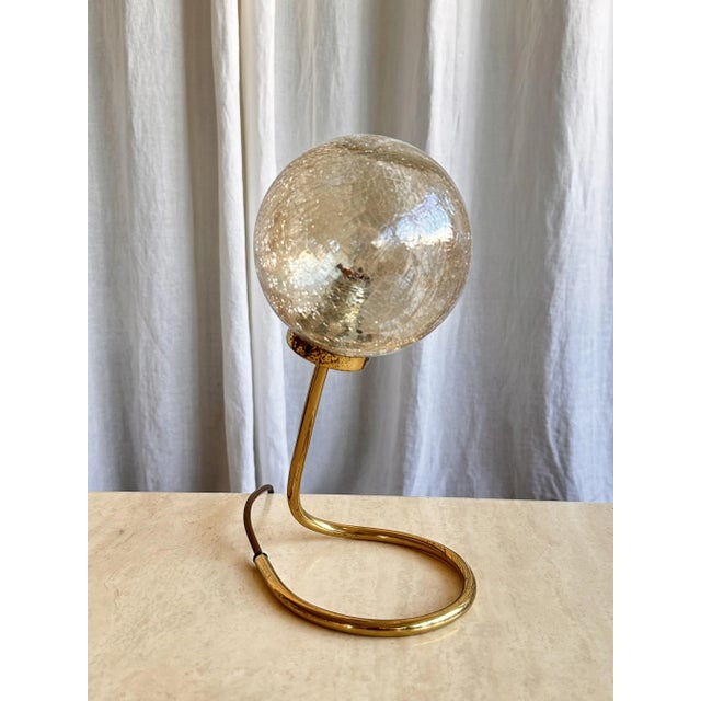 Wonderful table lamp with a spherical crackle glass shade and slender, tubular curling base. The shade has a light amber...