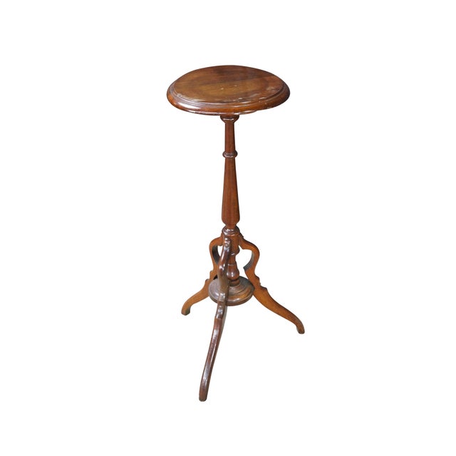 An antique Victorian mahogany torchère pedestal stand features a small, circular flat tabletop bordered by a simple...
