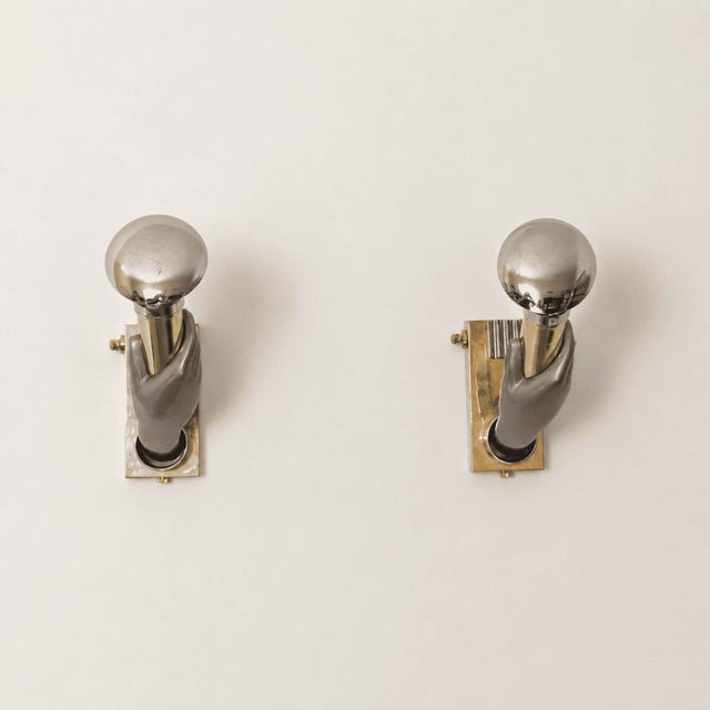 A pair of 1970s Italian wall lamps crafted from metal and brass, featuring a dramatic Gothic-style hand-shaped form. The...